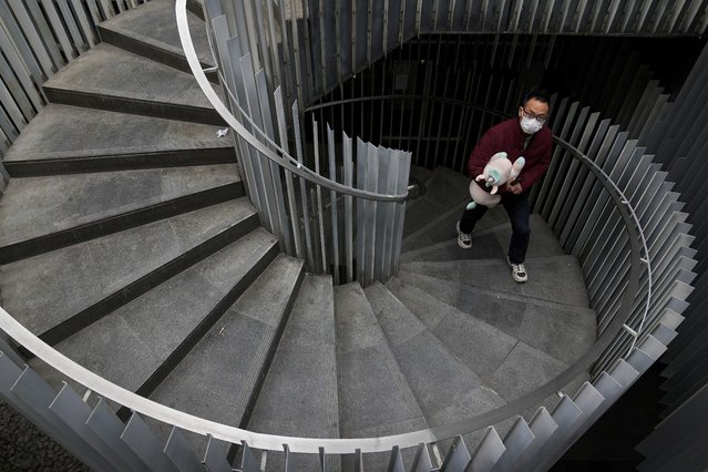 A man wearing a face mask to protect from COVID-19 holds a unicorn soft toy as he walks up an oval staircase at a commercial office building in Beijing, Sunday, November 28, 2021. (Photo by Andy Wong/AP Photo)