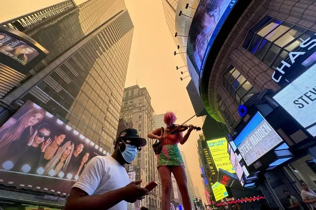 A performer plays the violin as a passerby wears a mask in Times Square as Manhattan is shrouded in haze and smoke which drifted south from wildfires in Canada, in New York City, New York, U.S., June 7, 2023. (Photo by Maye-E Wong/Reuters)