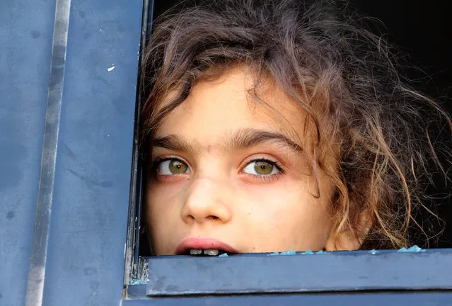 An evacuated Syrian girl from the area of Fuaa and Kafraya in the Idlib province, looks out of a broken bus window as it passes the al- Eis crossing south of Aleppo during the evacuation of several thousand residents from the two pro- regime towns in northern Syria on July 19, 2018. As the buses passed through rebel- held territory, people threw rocks at them, which shattered the windows during the evacuation which put an end to one of the longest sieges of the country' s seven- year civil war. Fuaa and Kafraya were the last remaining areas under blockade in Syria and a rare example of pro- government towns surrounded by rebel forces. (Photo by Ibrahim Yasouf/AFP Photo)