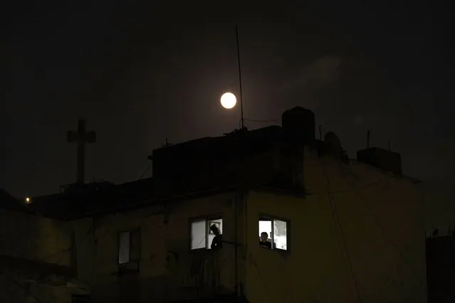 People look out from their apartment window as the July full moon, known as the Buck Moon, rises over the capital city of Beirut, Lebanon, Sunday, July 2, 2023. (Photo by Hassan Ammar/AP Photo)