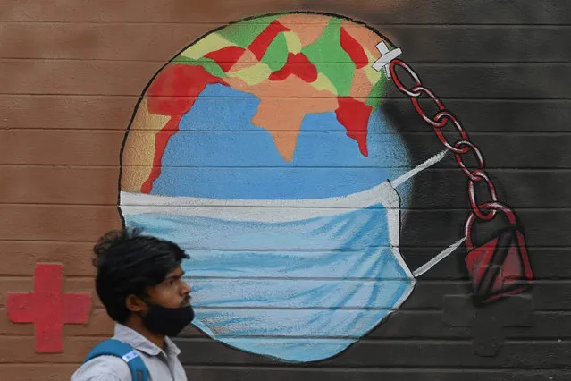 A pedestrian with his mask lowered walks past a wall mural depicting a world wearing a facemask as awareness measure against the Covid-19 coronavirus, in Mumbai on March 21, 2021. (Photo by Indranil Mukherjee/AFP Photo)