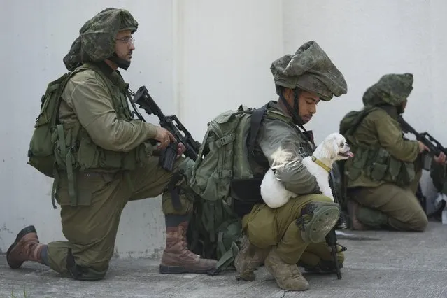 An Israeli soldier holds a dog in kibbutz Kfar Azza on Tuesday, October 10, 2023. Hamas militants overran Kfar Azza on Saturday, where many Israelis were killed and taken captive. (Photo by Erik Marmor/AP Photo)