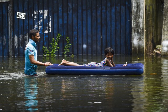 A man pushes a child laying on an inflatable mattress to make their way through floodwaters after heavy monsoon rains in Kelaniya, on the outskirts of Colombo on June 6, 2021. (Photo by Ishara S. Kodikara/AFP Photo)