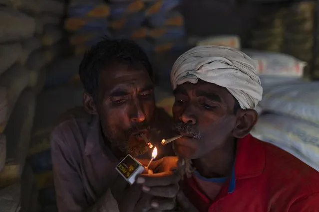 Workers who transport iron rods used in building construction light bidis as they take a break at a warehouse in Prayagraj, India, Thursday, July 29, 2021. (Photo by Rajesh Kumar Singh/AP Photo)