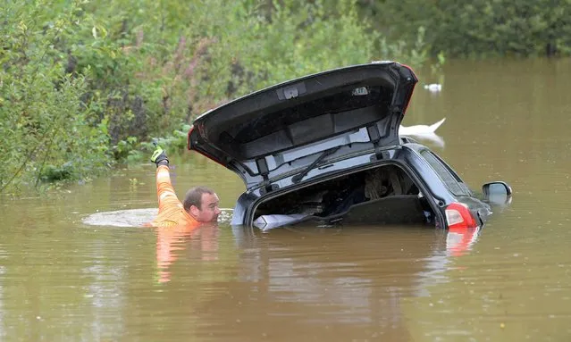 A rescue worker approaches a car partly submerged in water on Källviksvägen in Falun, Sweden, on August 18, 2021 after heavy rains in eastern Sweden caused flooding. (Photo by Ulf Palm/TT News Agency via AFP Photo)