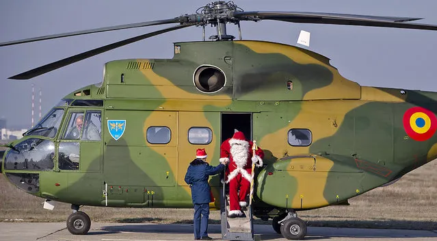 A man wearing a Santa Claus outfit receives help to exit a helicopter at the Romanian Airforce Base 90 in Otopeni, outside Bucharest, Romania, Tuesday, December 17, 2013. Santa arrived on a Puma helicopter and distributed gifts to the children of the Romanian air force personnel. (Photo by Vadim Ghirda/AP Photo)