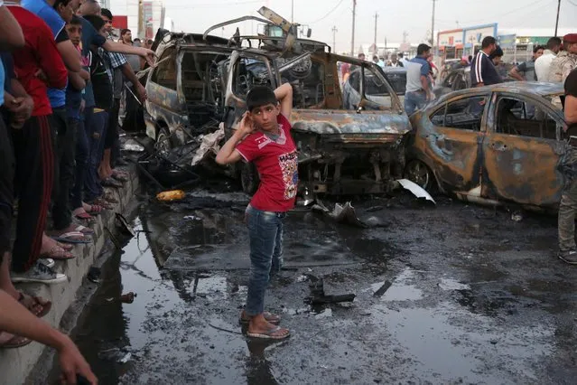 A boy watches as people and security forces gather at the scene of a car bomb explosion in Habibya in eastern Baghdad, Iraq, Friday, April 17, 2015. (Photo by Karim Kadim/AP Photo)