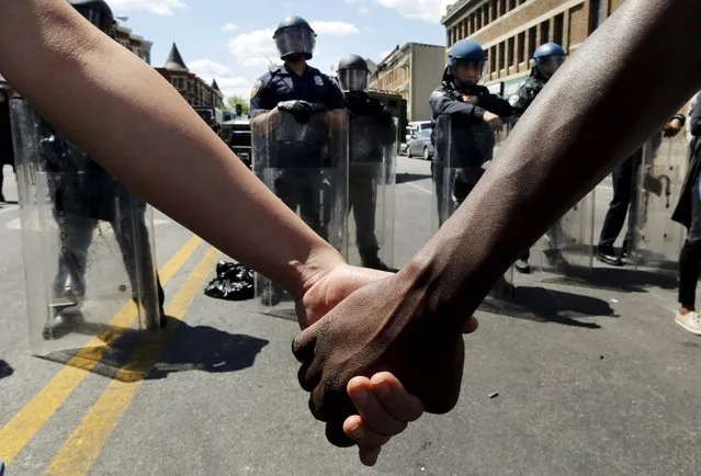 Members of the community hold hands in front of police officers in riot gear outside a recently looted and burned CVS store in Baltimore, Maryland, United States April 28, 2015. (Photo by Jim Bourg/Reuters)