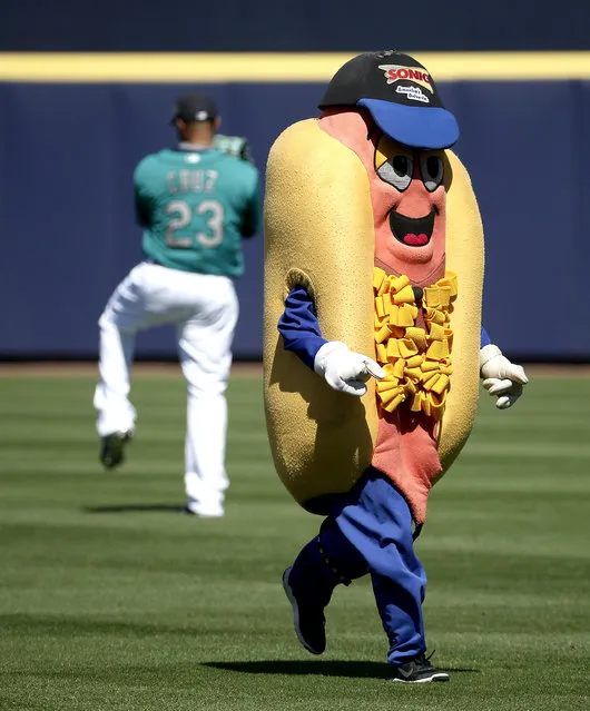 A mascot taking part in a race runs past Seattle Mariners' Nelson Cruz during the third inning of a spring training baseball game against the Kansas City Royals Wednesday, March 9, 2016, in Peoria, Ariz. (Photo by Charlie Riedel/AP Photo)