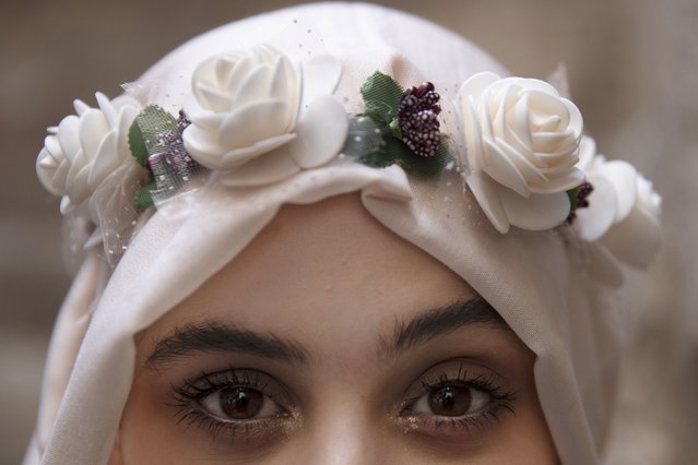 A young Palestinian woman wears a flower crown over her hijab and gold accents in her eye makeup in the Old City of Jerusalem on her way to prayers at the Al Aqsa Mosque compound marking Moulid al-Nabi, the birthday of the Prophet Muhammad, Tuesday, October 19, 2021. (Photo by Maya Alleruzzo/AP Photo)