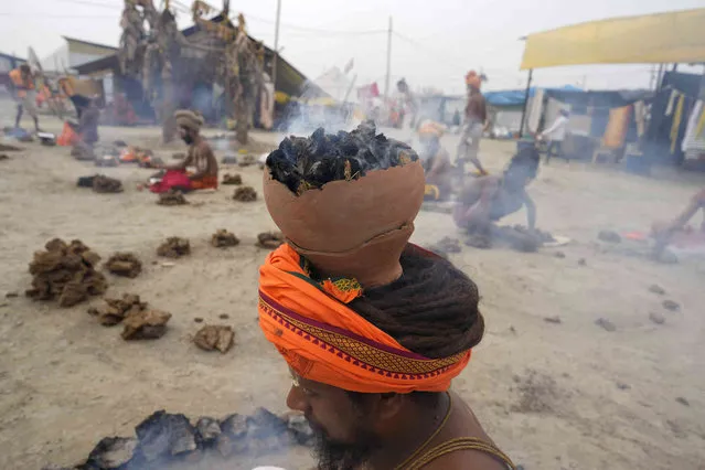 Hindu holy men, perform a ritual by burning dried cow dung cakes in earthen pots at the Sangam, the confluence of sacred rivers the Yamuna and the Ganges at the annual traditional fair of Magh Mela in Prayagraj, in the northern Indian state of Uttar Pradesh, India, Friday, February 16, 2024. Hundreds of thousands of devout Hindus bathe at the confluence during the astronomically auspicious period of over 45 days celebrated as Magh Mela. (Photo by Rajesh Kumar Singh/AP Photo)
