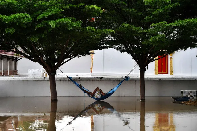 A man rests in a hammock in the grounds of a flooded Buddhist temple in the central Thai province of Ayutthaya on September 28, 2021, as tropical storm Dianmu caused flooding in 30 provinces across the country. (Photo by Lillian Suwanrumpha/AFP Photo)