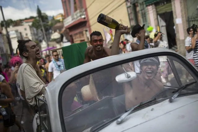 A reveler holds a bottle of sparkling wine as he drives a car at the “Ceu na Terra” block party during Carnival celebration in Rio de Janeiro, Brazil, Saturday, March 1, 2014. Rio de Janeiro's over-the-top Carnival is the highlight of the year for many local residents. Hundreds of thousands of merrymakers will take to Rio's streets in the nearly 500 open-air “bloco” parties. (Photo by Felipe Dana/AP Photo)