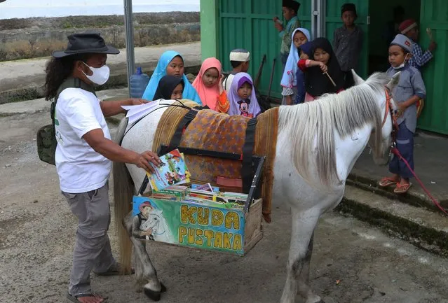 The initiator of Kuda Pustaka (Horse Library ) Ridwan Sururi (48) with a horse carrying books came to children who were waiting to be exchanged with the new titles that children needed in Pesanggrahan village, Purbalingga, Central Java on November, 4,2021. In a Unique Way, he never gets tired of distributing his 120 book titles with various titles brought by his horse with two baskets on both sides, even during the covid-19 pandemic. Ridwan Sururi carried out traveling activities carrying books aimed at increasing interest in reading residents, especially children so that they instill a hobby of reading books at a time when digital technology has mastered and now the collection of library horse books has seven thousand books collected from 2014 when they first started until now and has opened a library at home so that residents, children, and students can visit and borrow books with various book titles as needed. (Photo by Dasril Roszandi/Anadolu Agency via Getty Images)