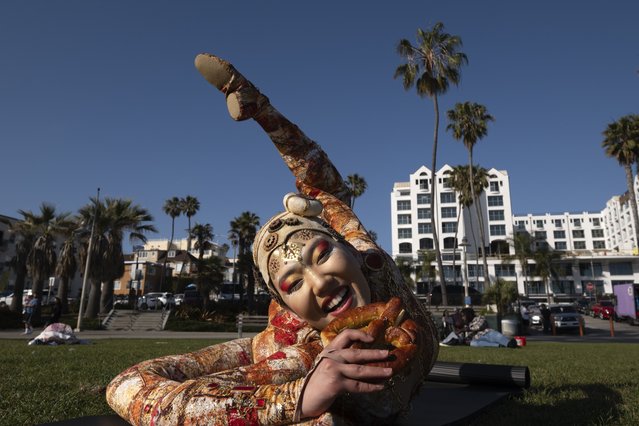 Cirque du Soleil contortionist Sender Enkhtur takes a bite on a pretzel as she poses for a photo at Santa Monica Beach, Monday, April 29, 2024, in Santa Monica, Calif. Cirque du Soleil announced their return to the Santa Monica Pier this fall after being gone for over a decade. (Photo by Richard Vogel/AP Photo)