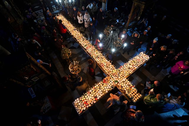 Believers light candles on a cross-shaped platform covered with candles attached to jars of honey during a ceremony marking the day of Saint Haralampi, Orthodox patron saint of beekeepers, at the Church of the Blessed Virgin in Blagoevgrad, eastern Bulgaria, on February 10, 2023. (Photo by Nikolay Doychinov/AFP Photo)