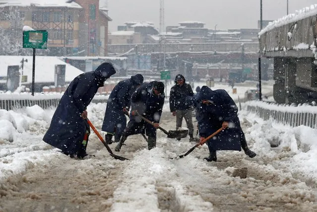 Municipal workers use shovels to remove snow from road during a snowfall in Srinagar on February 23, 2022. (Photo by Danish Ismail/Reuters)