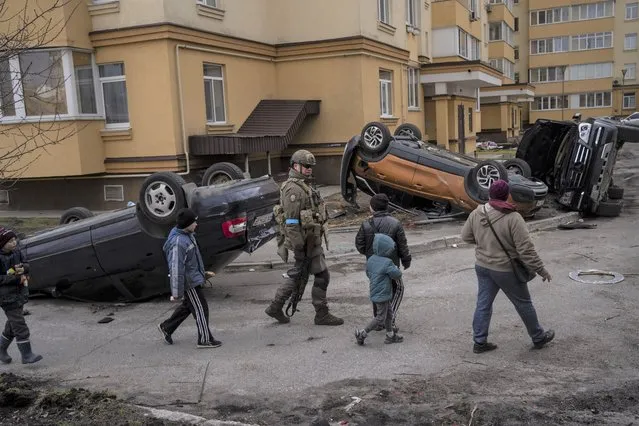A Ukrainian soldier walks with children passing destroyed cars due to the war against Russia, in Bucha, on the outskirts of Kyiv, Ukraine, Monday, April 4, 2022. (Photo by Rodrigo Abd/AP Photo)