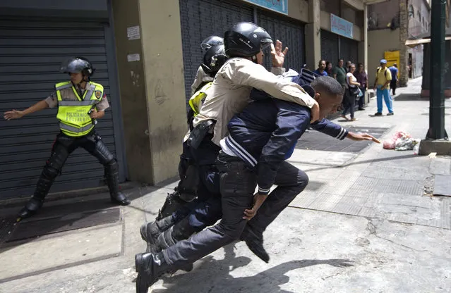 A National Bolivarian Police officer rescues a man who was being attacked by protesters, who then threw rocks at them, during a protest demanding food a few blocks from Miraflores presidential palace in Caracas, Venezuela, Thursday, June 2, 2016. (Photo by Fernando Llano/AP Photo)