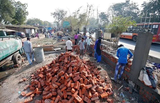 Construction workers build a wall along a slum area as part of a beautification drive along a route that U.S. President Donald Trump and India's Prime Minister Narendra Modi will be taking during Trump's visit later this month, in Ahmedabad, India, February 13, 2020. (Photo by Amit Dave/Reuters)