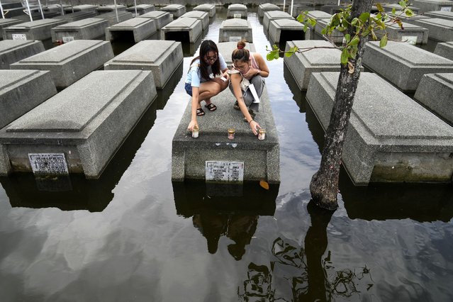 Women place candles on the half-submerged tomb of family members at flood-prone Holy Spirit Memorial Park in Masantol, Pampanga province, Philippines after heavy rains from recent tropical storm Trami caused water to become higher than usual, ahead of All Saints Day, Thursday October 31, 2024. (Photo by Aaron Favila/AP Photo)