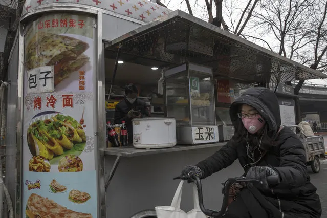 A masked bicyclist passes by a breakfast stand in the central business district in Beijing Monday, March 9, 2020. With almost no new COVID-19 cases being reported in Beijing, workers are slowly returning to their offices with masks on and disinfectant in hand. But officials remain cautious, torn between wanting to restart the economy and fear of a resurgence of the outbreak. (Photo by Ng Han Guan/AP Photo)