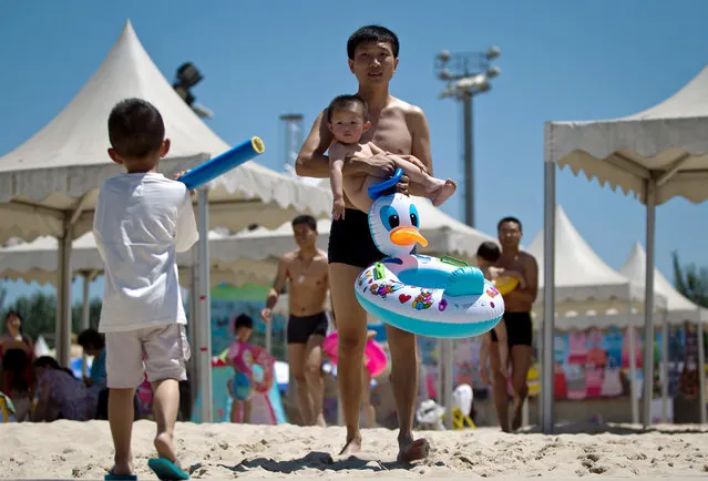 A man carries a child across a manmade beach at a park during summer in Beijing, on June 16, 2012. (Photo by Andy Wong/AP Photo)