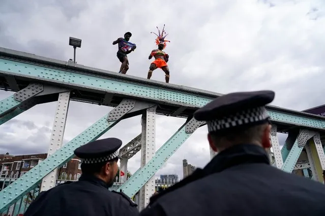 Police officers watch as revellers dance on top of a railway bridge during the annual Notting Hill Carnival in west London, Monday, August 29, 2022. The carnival which returned to the streets for the first time in two years, after it was thwarted by the pandemic, is one of the largest festival celebrations of its kind in Europe. (Photo by Alberto Pezzali/AP Photo)