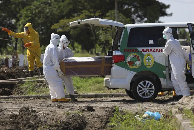 Health workers unload a plastic-wrapped coffin containing the body of a coronavirus victim from an ambulance for burial at a cemetery in Surabaya, East Java, Indonesia, Thursday, April 23, 2020. (Photo by Trisnadi/AP Photo)