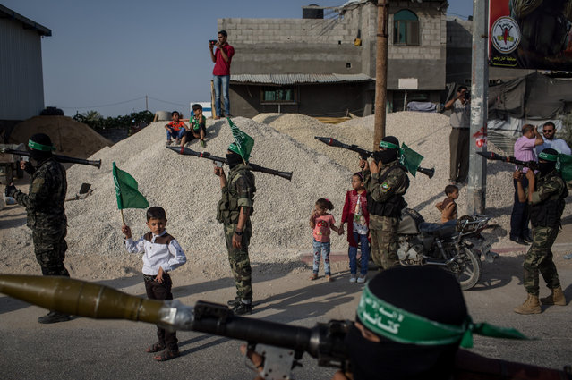 A young boy holds up a Hamas flag in between Palestinian Hamas militant during a military show in the Bani Suheila district on July 20, 2017 in Gaza City, Gaza. For the past ten years Gaza residents have lived with constant power shortages, in recent years these cuts have worsened, with supply of regular power limited to four hours a day. On June 11, 2017 Israel announced a new round of cuts at the request of the Palestinian authorities and the decision was seen as an attempt by President Mahmoud Abbas to pressure Gaza's Hamas leadership. Prior to the new cuts Gaza received 150 megawatts per day, far below it's requirements of 450 megawatts. In April, Gaza's sole power station which supplied 60 megawatts shut down, after running out of fuel, the three lines from Egypt, which provided 27 megawatts are rarely operational, leaving Gaza reliant on the 125 megawatts supplied by Israel's power plant. The new cuts now restrict electricity to three hours a day severely effecting hospital patients with chronic conditions and babies on life support. During blackout hours residents use private generators, solar panels and battery operated light sources to live. June 2017 also marked ten years since Israel began a land, sea and air blockade over Gaza. Under the blockade, movement of people and goods is restricted and exports and imports of raw materials have been banned. The restrictions have virtually cut off access for Gaza's two million residents to the outside world and unemployment rates have skyrocketed forcing many people into poverty and leaving approximately 80% of the population dependent on humanitarian aid. (Photo by Chris McGrath/Getty Images)