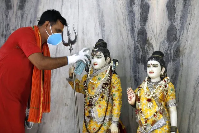 An Indian priest sanitizes the idol of Lord Shiva and Godess Parvati at a temple, in Prayagraj, India, Monday, June 8, 2020. Religious places, malls, hotels and restaurants open Monday after more than two months of lockdown as a precaution against coronavirus. (Photo by Rajesh Kumar Singh/AP Photo)
