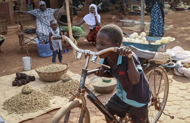 In this May 13, 2020, photo, a boy pushes his bicycle past food stalls at a market in Tougan, Burkina Faso. Violence linked to Islamic extremists has spread to Burkina Faso's breadbasket region, pushing thousands of people toward hunger and threatening to cut off food aid for millions more. (Photo by Sam Mednick/AP Photo)