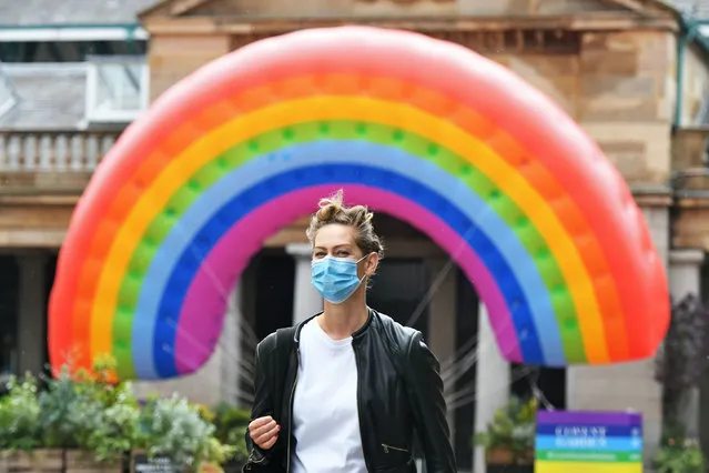A woman wearing a facemask walks past a large rainbow in Covent Garden, London on June 19, 2020, after the UK's chief medical officers agreed to downgrade the coronavirus alert level from four to three after a “steady” and continuing decrease in cases in all four nations. (Photo by Dominic Lipinski/PA Images via Getty Images)