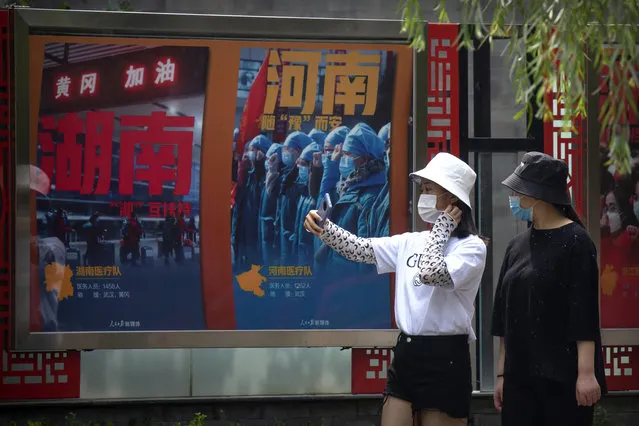 People wearing face masks to protect against the new coronavirus take photos near billboards honoring medical workers who responded to the coronavirus outbreak in Wuhan at a public park in Beijing, Friday, June 26, 2020. China reported a further decline in new cases Friday with about a dozen mostly in Beijing, where mass testing has been done following an outbreak that appears to have been largely brought under control. (Photo by Mark Schiefelbein/AP Photo)