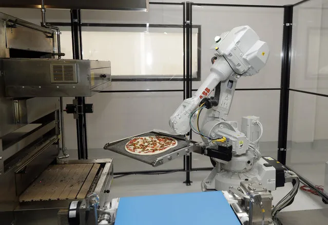 In this Monday, August 29, 2016 photo, a robot places a pizza into an oven at Zume Pizza in Mountain View, Calif. The startup, which began delivery in April, is using intelligent machines to grab a slice of the multi-billion-dollar pizza delivery market. Zume is one of a growing number of food-tech firms seeking to disrupt the restaurant industry with software and robots that let them cut costs, speed production and improve worker safety. (Photo by Marcio Jose Sanchez/AP Photo)