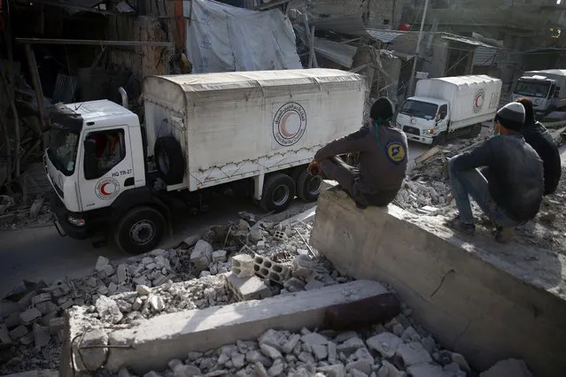 Civil defence members sit amid the rubble as they watch an aid convoy of Syrian Arab Red Crescent driving through the besieged town of Douma, Eastern Ghouta, Damascus, Syria on March 5, 2018. (Photo by Bassam Khabieh/Reuters)