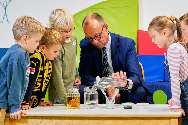 German Chancellor Friedrich Merz observes an experiment with children during his visit of a kindergarten in Potsdam, Germany, Tuesday, October 14, 2025. (Photo by Markus Schreiber/AP Photo)
