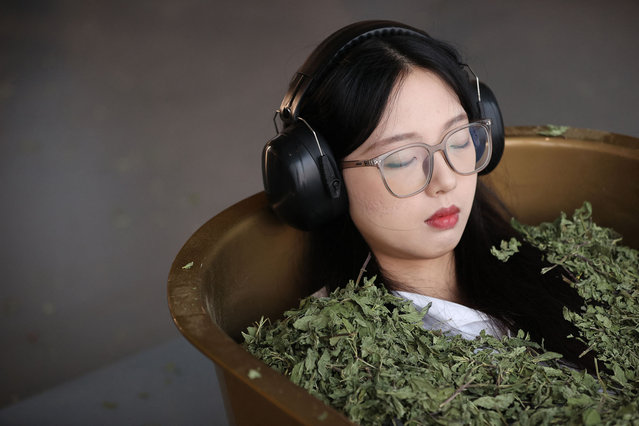 A visitor submerge lies in a tub filled with dried leaves, as part of an interactive artwork by Serbian conceptual artist Marina Abramovic on the opening day of her first exhibition in China – titled “Transforming Energy” – in Shanghai on October 11, 2024. (Photo by AFP Photo/China Stringer Network)