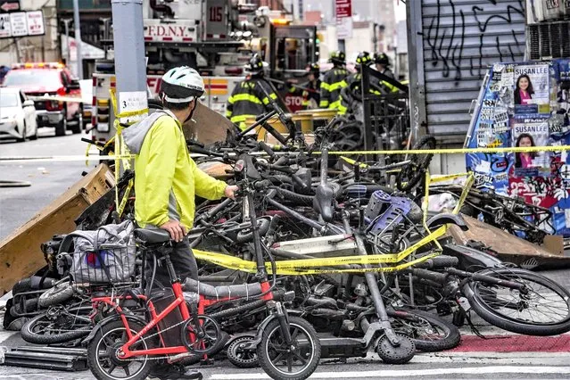 A biker stops to look at a pile of e-bikes in the aftermath of a fire in Chinatown, which authorities say started at an e-bike shop and spread to upper-floor apartments, Tuesday June 20, 2023, in New York. (Photo by Bebeto Matthews/AP Photo)