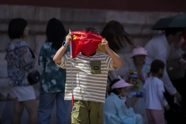 A boy uses a national flag to shield from the sun as visitors line up to enter the Forbidden City on a sweltering day in Beijing, Friday, July 7, 2023. (Photo by Andy Wong/AP Photo)