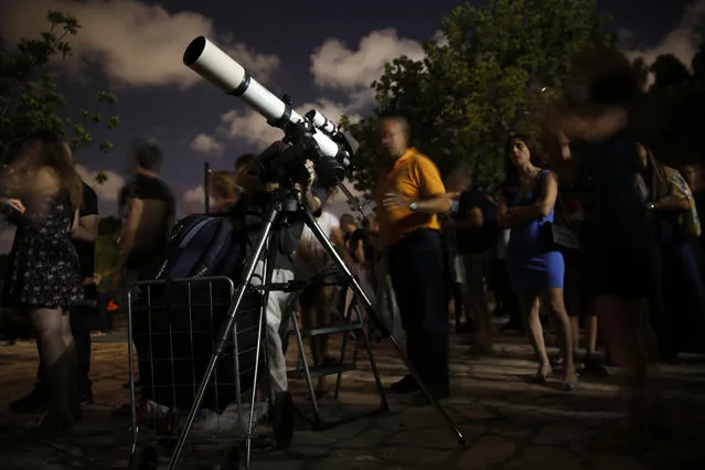 People watch the moon turn red during a lunar eclipse in Giv'atayim, Israel, Friday, July 27, 2018. Skywatchers around much of the world are looking forward to a complete lunar eclipse that will be the longest this century. (Photo by Ariel Schalit/AP Photo)