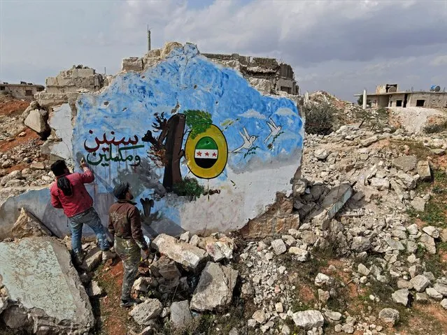 Syrians paint a mural on the remains on a building in the rebel held town of Binnish in Syria's northwestern province of Idlib, on March 11, 2021, marking the 10-years of the Syrian war. (Photo by Rami Al Sayed/AFP Photo)