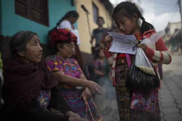 In this June 20, 2018 photo, a girl reads a paper announcing the National Day of Forced Disappearance during a funeral ceremony for 172 unidentified people who were dug up from a former military base, one day before properly burying them in the same area they were discovered, in San Juan Comalapa, Guatemala. The United Nations has documented the disappearance of 45,000 people during the 36 years of civil war in Guatemala, and the murder of another 200,000. (Photo by Rodrigo Abd/AP Photo)