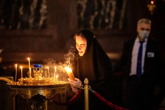 An orthodox nun lights candles during a service marking the Holiday of Annunciation in the Cathedral of Christ the Saviour in Moscow, on April 7, 2021. In Christianity, Annunciation celebrates the revelation to the Virgin Mary that she would bear a son, Jesus. (Photo by Dimitar Dilkoff/AFP Photo)