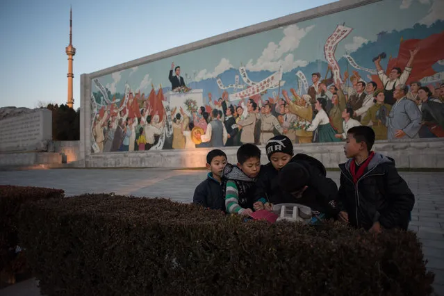 Children write in a book after cleaning the area in front of a propaganda mosaic in Pyongyang on December 1, 2016. (Photo by Ed Jones/AFP Photo)