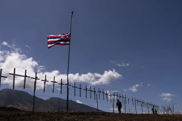 Crosses honoring the victims killed in a recent wildfire hang on a fence along the Lahaina Bypass as a Hawaiian flag flutters in the wind in Lahaina, Hawaii, Tuesday, August 22, 2023. Two weeks after the deadliest U.S. wildfire in more than a century swept through the Maui community of Lahaina, authorities say anywhere between 500 and 1,000 people remain unaccounted for. (Photo by Jae C. Hong/AP Photo)