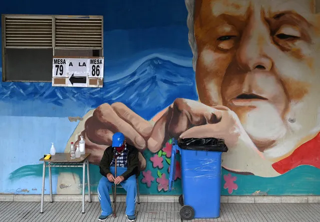 An elderly man waits in front of a mural outside a polling station during elections to choose mayors, councillors and a commission to rewrite the constitution in Santiago, on March 15, 2021. (Photo by Rodrigo Arangua/AFP Photo)