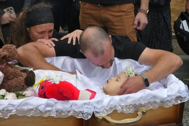 Artem Dmitriev gives the last salute to his daughter Liza, 4-year-old girl killed by Russian attack, in Vinnytsia, Ukraine, Sunday, July 17, 2022. Wearing a blue denim jacket with flowers, Liza was among 23 people killed, including two boys aged 7 and 8, in Thursday's missile strike in Vinnytsia. Her mother, Iryna Dmytrieva, was among the scores injured. (Photo by Efrem Lukatsky/AP Photo)