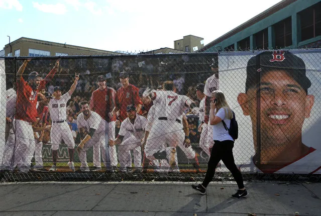 A woman walks by large photo scrims hanging outside Fenway Park showing Boston Red Sox players and manager Alex Cora, Wednesday, October 10, 2018, in Boston. Game 1 of the baseball American League Championship Series between the Red Sox and the Houston Astros is scheduled for Saturday in Boston. (Photo by Elise Amendola/AP Photo)
