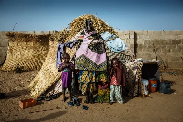 A woman stands with her grandchildren outside of the small straw house, where they all live. The family fled their village months earlier, when it was attacked by Boko Haram, and now live in a host community in Maiduguri, Nigeria. (Photo by Muse Mohammed/IOM)